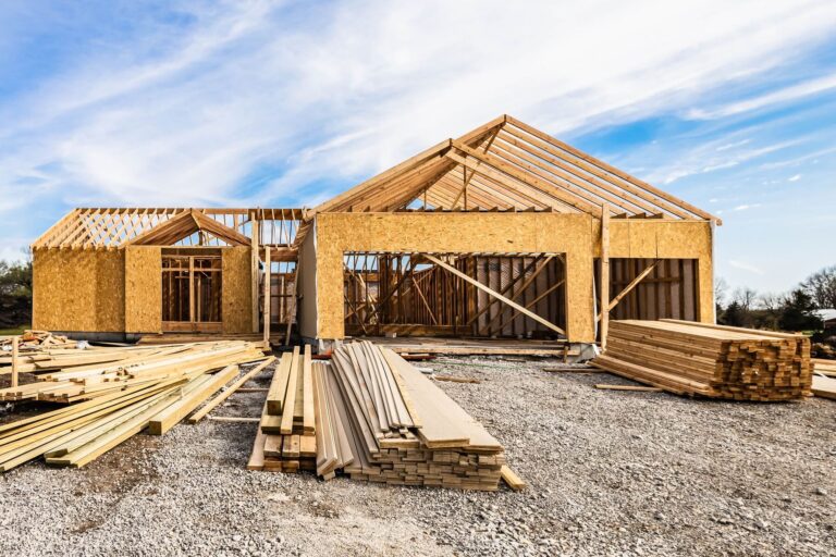 New house under construction, front view from garage door entry with clouds blue sky. Framing of home exterior structure with a pile of lumber and siding plank leftover. Real estate business industry.